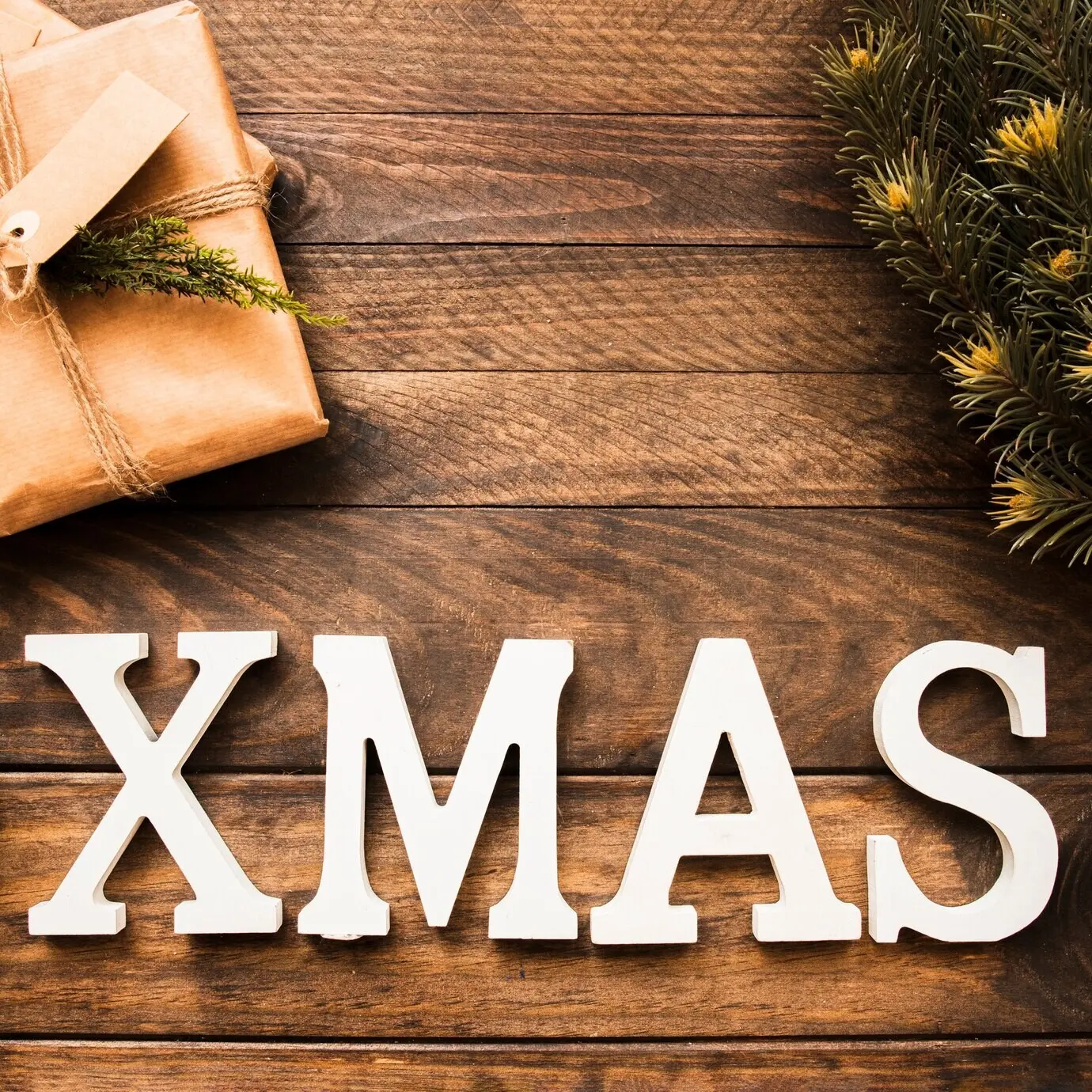 Xmas-Schriftzug neben einem Nadelzweig und einer Geschenkbox.